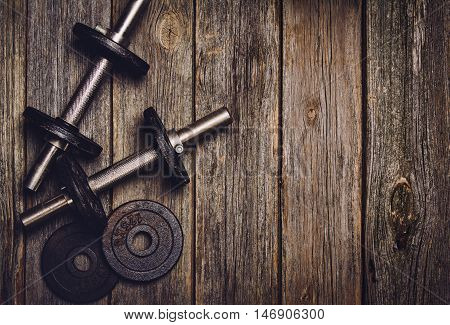 Old iron dumbbells or exercise weights with extra plates on an old wooden deck, floor or table. Image taken from above, top view. A lot of copy space around product