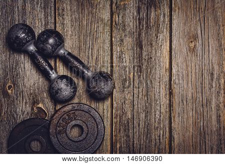Old iron dumbbells or exercise weights with extra plates on an old wooden deck, floor or table. Image taken from above, top view. A lot of copy space around product