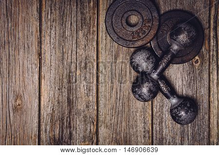 Old iron dumbbells or exercise weights with extra plates on an old wooden deck, floor or table. Image taken from above, top view. A lot of copy space around product