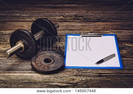 Old iron dumbbells or exercise weights with extra plates on an old wooden deck, floor or table. Image taken from above, low angle . A lot of copy space around product