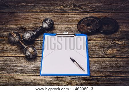 Old iron dumbbells or exercise weights with extra plates on an old wooden deck, floor or table. Image taken from above, low angle . A lot of copy space around product
