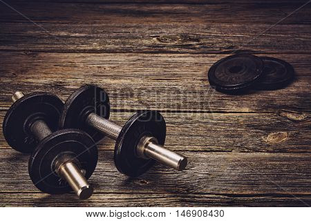 Old iron dumbbells or exercise weights with extra plates on an old wooden deck, floor or table. Image taken from above, low angle . A lot of copy space around product