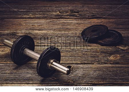 Old iron dumbbells or exercise weights with extra plates on an old wooden deck, floor or table. Image taken from above, low angle . A lot of copy space around product