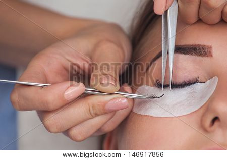 Makeup Master corrects and strengthens eyelashes beams holding out a pair of tweezers in a beauty salon. Professional care for the skin and eyes.
