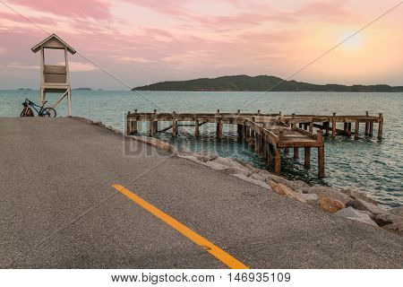 Lifeguard house near calm abandoned jetty and sunset .