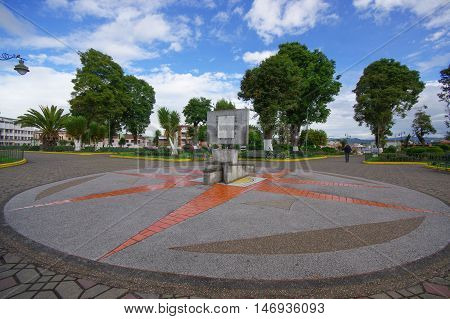 TULCAN, ECUADOR - JULY 3, 2016: cardinal points monument in the middle of the park with some trees as background.