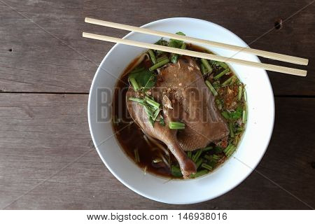 The stewed duck thigh noodles in brown soup with bamboo chopsticks .