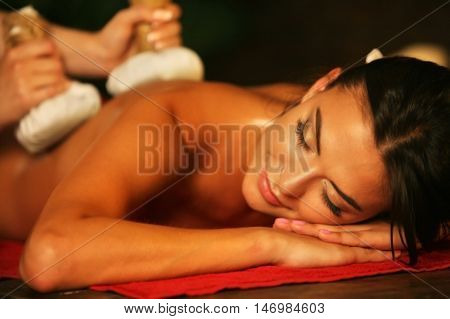 Young woman lying on wooden spa bed. Poultice hot herbal massage in spa salon.