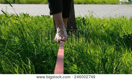 Woman Legs Walk Along A Tight Line In The Park. Foot Woman Balances On The Slackline Close Up.
