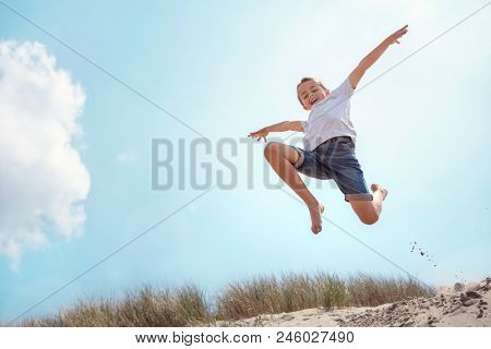Boy leaping and jumping over sand dune on beach vacation
