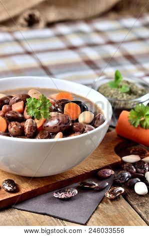 Bowl Of Bean Soup With Large Beans On Cutting Board, Carrots, Parsley, Marjoram, Spoon And Ladle, To