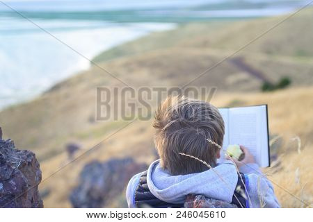 Boy Reading Book Outside On The Top Of The Hill, Up Above The Ocean, Unschooling Education
