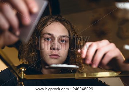 Conceptual close-up portrait of a teenager affected by drug abuse staring while preparing powdered cocaine for snorting at home