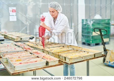 Confectionery Factory Employee In White Coat Squeezing Red Cream From Pastry Bag.