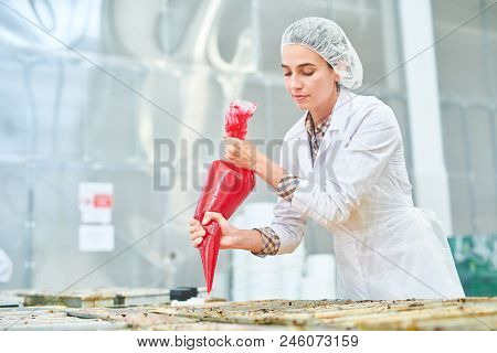Beautiful Confectionery Factory Worker In White Coat Squeezing Red Cream From Pastry Bag.