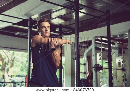 Waist-up Portrait Of Sporty Handsome Man Looking Away While Doing Stretching Exercise For Arms, Inte