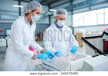 Confectionery Factory Employees In White Coats Packing Paper Box With Pastry Into Plastic Film.