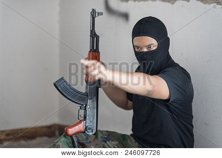 Black Masked Robber In The Black Shirt And Camouflage Pant Is Sitting On The Floor And Hold The Gun 