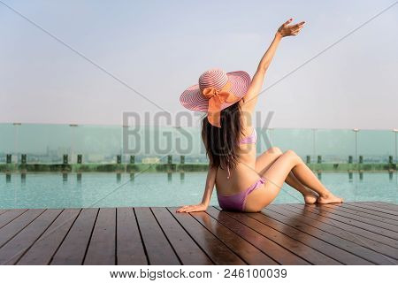 Asian Sexy Woman Raise Hand In Bikini And Hat Was Sitting Near The Pool And Enjoying Her Vacation In