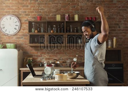 African-american Man In Earphones Listening To Music And Dancing While Baking In Kitchen