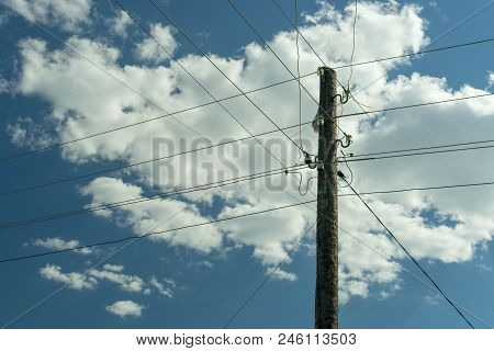 Old Wooden Power Post Column Entangled With Live Wires Against The Blue Sky With Clouds
