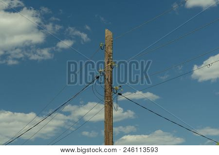 Old Wooden Power Pole Entangled Wires With Electricity, Against A Blue Sky Background