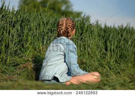 Alone Blond Hair Young Girl Sits On Path, On Her Back, Dressed In Jeans Blue Jacket And Shorts, Has 