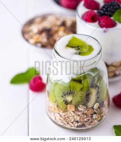 White Yogurt With Muesli In Glass Bowl With Pieces Of Kiwi On Top And Whole Pieces On The Right Side