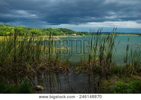 View On The Dock Behind Grass Along The Lake Shore With Dark Blue Cloudscape And Sunshine, El Remate