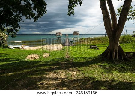 Dock With Hammocks Along The Lake Shore With Boat And Dark Blue Cloudscape And Sunshine, El Remate, 