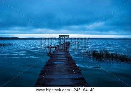 Pier Dock Leading To Hut Along The Lake Shore Before Sunset In Blue, El Remate, Peten, Guatemala
