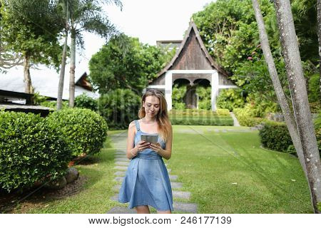 Young Woman Using Smartphone And Standing With Resort House In Background. Concept Of Modern Technol