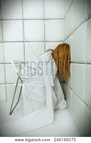 Portrait of a crazy girl dressed in a straitjacket in an isolated room in a madhouse.
