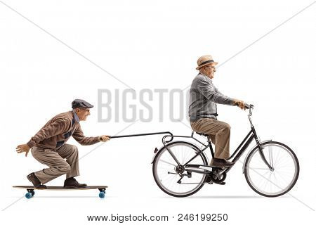 Senior riding a bike with another senior riding a longboard and pulling himself with a cane isolated on white background
