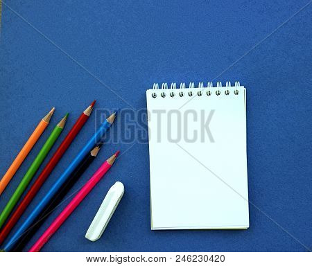 Stationery For School On A Blue Background. Notepad, A Set Of Colored Pencils, Scissors, An Eraser. 