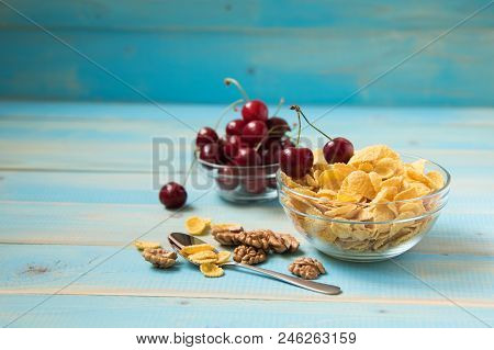 Tasty Cornflakes With Walnut And Cherry In Glass Bowl On Blue Background. Corn Flakes. Ealthy Breakf