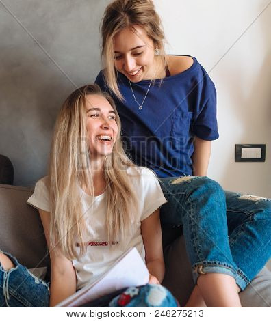 Two Young Girls Sitting On A Couch Watching Magazine