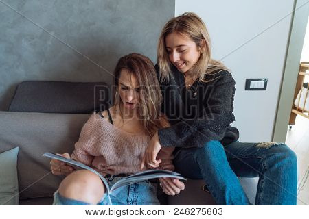 Two Young Girls Sitting On A Couch Watching Magazine