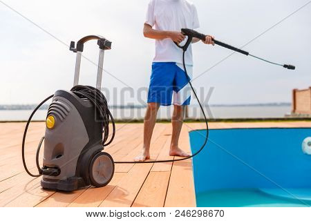A Man Is Cleaning A Swimming Pool With The Hepl Of A Vacuum Cleaner.