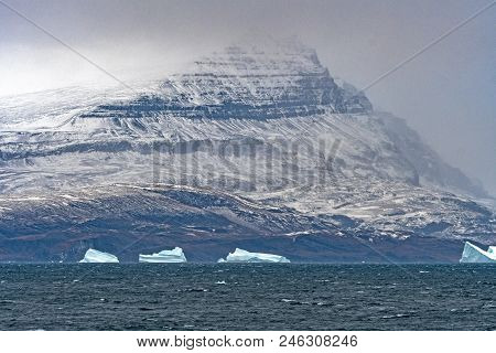 Coastal Mountain Looming Through The Clouds On A Remote Coast Of Greenland