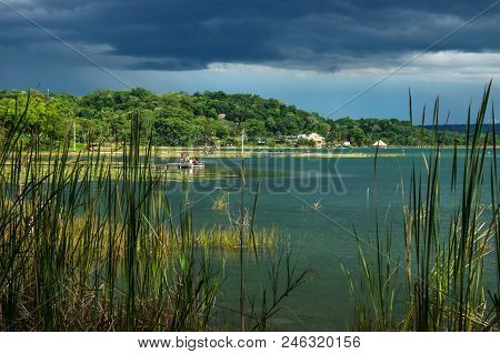 View On The Village With Dock Along The Lake Shore With Dark Blue Cloudscape And Sunshine, El Remate