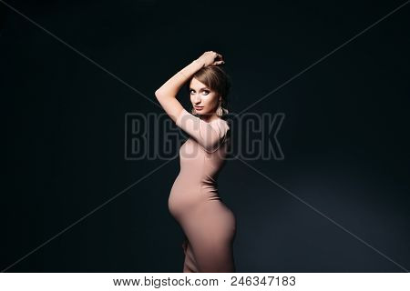 Portrait Of Pegnant Female, Waiting For A Baby, Posing At Dark Studio With Hand Up, Looking At Camer