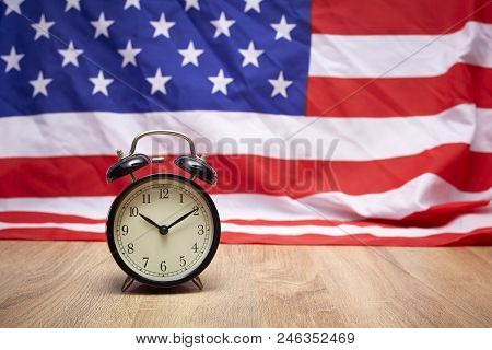 National Flag Of America And Black Alarm Clock On Old Wooden Background