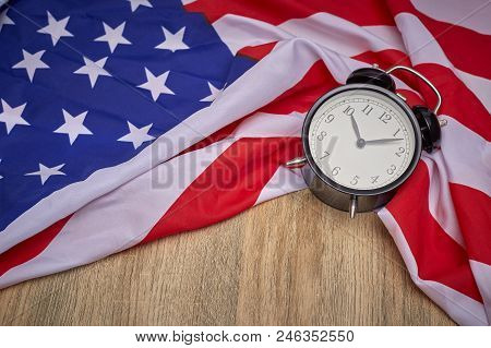 National Flag Of America And Black Alarm Clock On Old Wooden Background