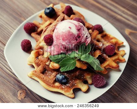 Plate of belgian waffles with ice cream and fresh berries - raspberries and blueberries.
