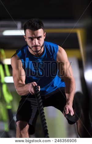 young fit athlete man working out in functional training gym doing  battle ropes exercise as part of cross fitness training