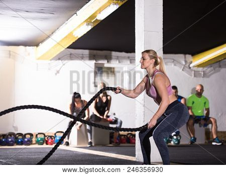 young fit athlete woman working out in functional training gym doing  battle ropes exercise as part of cross fitness training