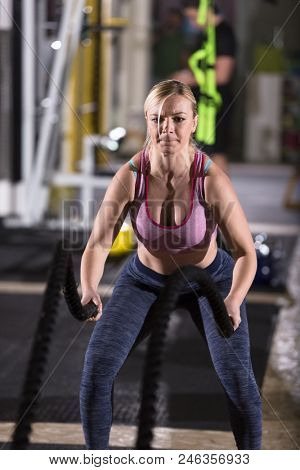young fit athlete woman working out in functional training gym doing  battle ropes exercise as part of cross fitness training