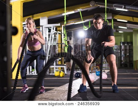young fit sports couple working out in functional training gym doing  battle ropes cross fitness exercise