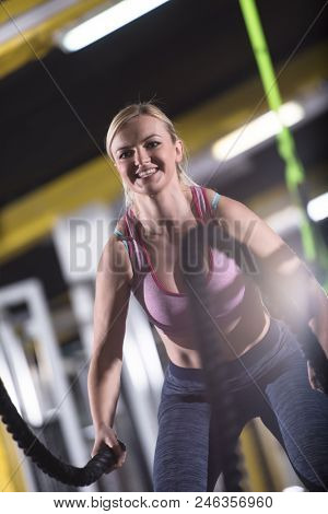 young fit athlete woman working out in functional training gym doing  battle ropes exercise as part of cross fitness training